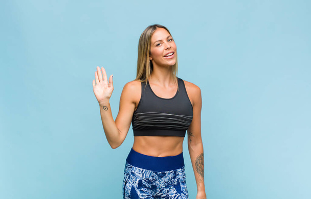 young pretty woman smiling happily and cheerfully, waving hand, welcoming and greeting you, or saying goodbye. fitness concept - Fotoğraf, Görsel
