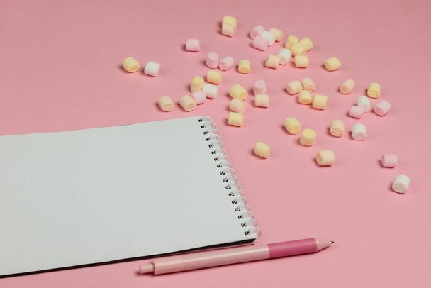 Quaderno con penna e tanti marshmallow sullo sfondo rosa pastello. Vista dall'alto - Foto, immagini