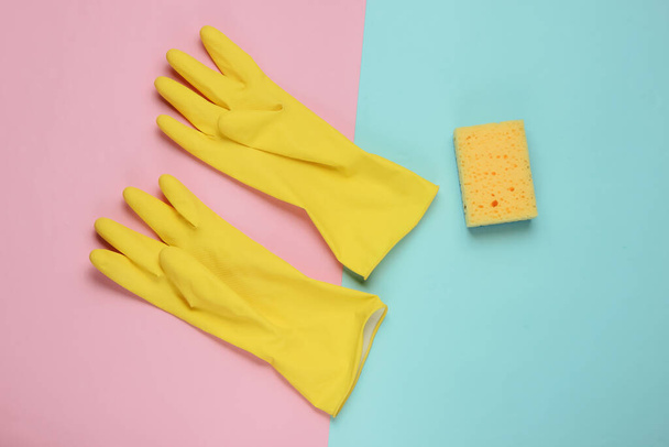 Gele latex handschoenen en spons voor reiniging op roze blauwe achtergrond. Het concept van schoonmaken. Pastel kleur trend. Een studio opname. Bovenaanzicht - Foto, afbeelding