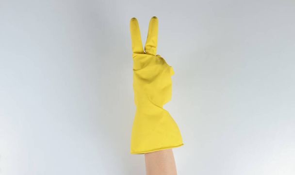 Mano en guantes de goma para la limpieza muestra gesto V sobre un fondo gris. - Foto, imagen