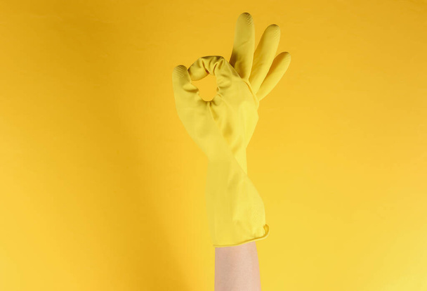 Koncept úklidu domu. Ženské ruce nosí žluté gumové rukavice pro čištění ukazuje gesto v pořádku na žlutém pozadí - Fotografie, Obrázek
