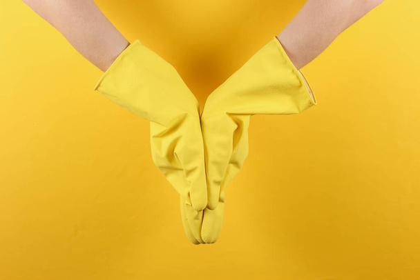 Manos femeninas en guantes de goma amarillos sobre fondo amarillo estudio. Concepto de limpieza - Foto, imagen