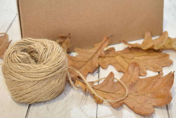 Cardboard box, autumn oak leaves and a ball of rope on the background of a wooden table top. Concept: seasonal delivery, packaging, natural eco-friendly products. Space for text. - Foto, Imagem