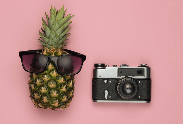 Nyári háttér. Szórakozás és humor. Utazási koncepció. Ananász napszemüveggel retro kamera rózsaszín pasztell háttérrel. Felülnézet - Fotó, kép