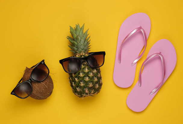 Summer background. Fun and humor concept. Beach resort. Pineapple and coconut with sunglasses, flip flopson yellow background - Zdjęcie, obraz