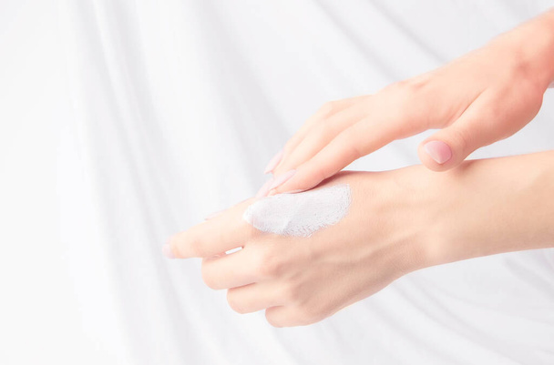 O conceito de cosméticos e cuidado de rosto e corpo. Mãos de mulheres com a nata em um contexto branco. Espaço de cópia - Foto, Imagem