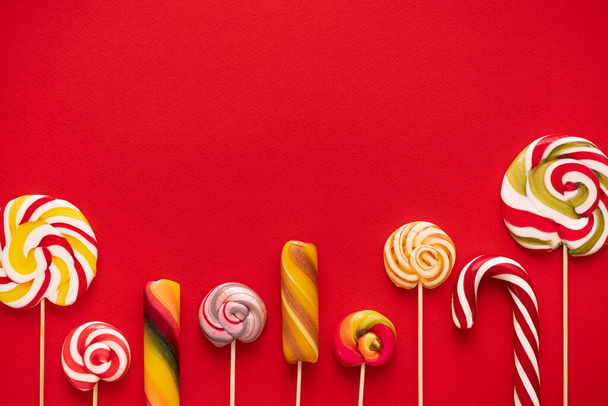 Zoete kleurrijke lolly pops op rode achtergrond. Lekkere kleur voedsel concept. Bovenaanzicht. Pop Art. - Foto, afbeelding