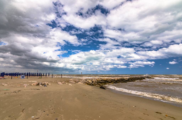 Seaside with closed umbrellas and cloudy sky - Фото, зображення