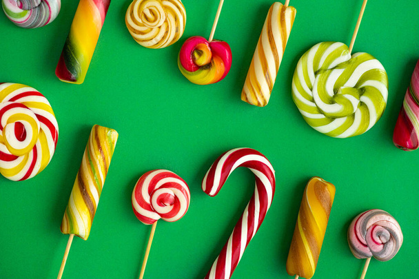 Sabroso caramelo lollypops diferentes colores sobre un fondo verde. Concepto de arte pop. Vista desde arriba. - Foto, imagen