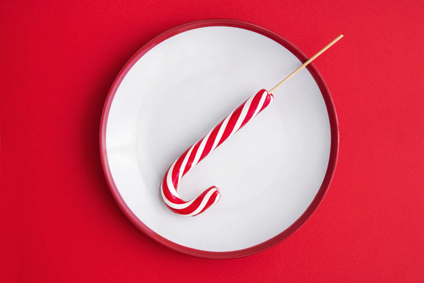 Christmas candy cane on a plate, red background. concept of sweet diet. top view. - Photo, Image