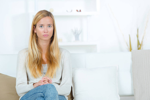 portrait of serious young woman sat alone on sofa - Photo, Image