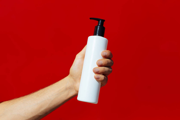 Man holding a white bottle isolated on a red background.Man hand holding a bottle (on red background) - Photo, Image