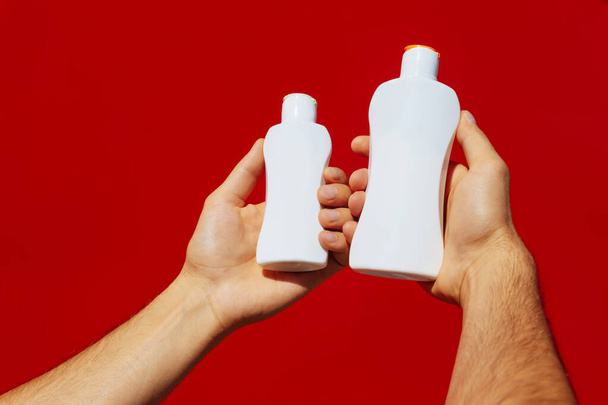 Dos manos sosteniendo botellas de plástico blanco sobre un fondo rojo. Frascos de plástico blanco - Foto, imagen