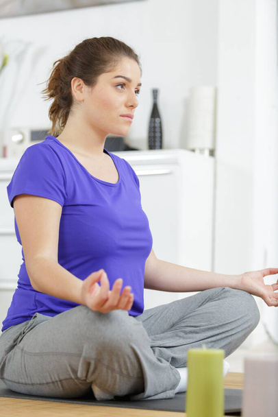 woman sitting on the floor of living room meditating - Фото, изображение