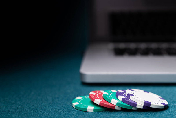 Színes póker zseton pénzt ezüst modern laptop egy kaszinó asztalon.  - Fotó, kép