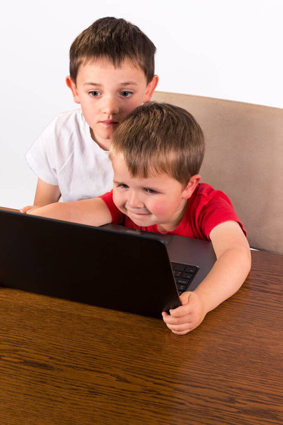 4-річний малюк розважається на портативному комп'ютері, а його старший брат спостерігає за своїм плечем. високий кут зору ізольований на білому тлі
 - Фото, зображення