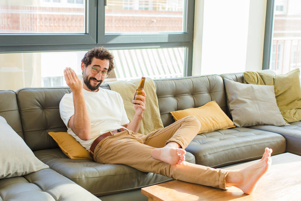 fiatal szakállas hűvös férfi ül egy kanapén otthon - Fotó, kép