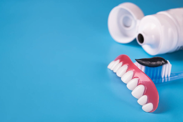 Black charcoal toothpaste on a toothbrush, model jaw denture, blue background. - Photo, Image
