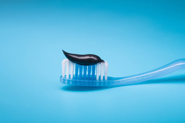 Черная древесный уголь зубная паста на зубной щетке, синий фон. - Фото, изображение