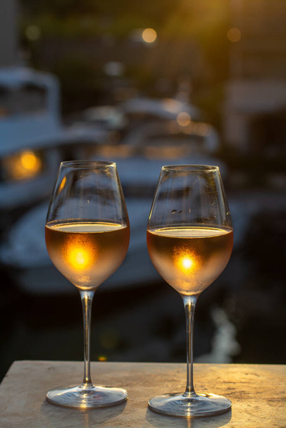 Degustacja lokalnego zimnego wina różanego w lecie na zachodzie słońca z łodzi żaglowych raju Port Grimaud na tle, Prowansja, Var, Francja - Zdjęcie, obraz