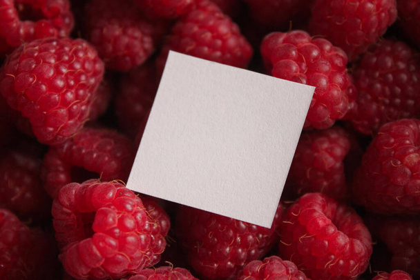 White sheet of paper for text on the background of ripe large red raspberries. Copy space. - Photo, Image