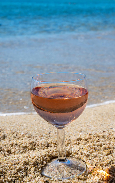 Copa de vino de rosas local en la playa de arena blanca y el mar Mediterráneo azul en el fondo, cerca de Le Lavandou, Var, Provenza, Francia - Foto, Imagen