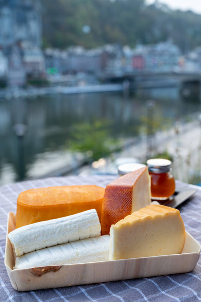 Cheese collection, tasty Belgian abbey cheeses made with brown trappist beer and fine herbs and view on Maas river in Dinant, Wallonia, Belgium - Photo, Image