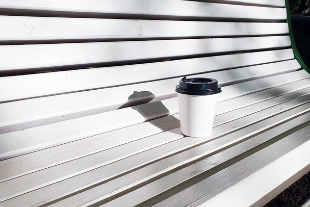 Mockup of white paper cup with  black lid on white wooden bench. Take-away cup with plastic lid. - Foto, Imagem