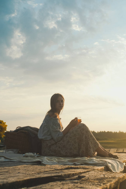 Pohled na dívku snů sedící na molu na jezeře a snění. Východ slunce nad jezerem. Horký čaj, konvice a sladkosti štěstí nebo inspirace koncepce, Užijte si život. Fotografie s efektem filmu a obilí - Fotografie, Obrázek
