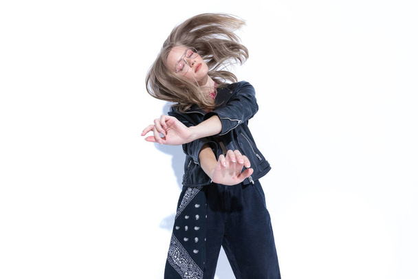 Dreaming fashion model dancing, wearing glasses and leather jacket on white studio background - Foto, imagen