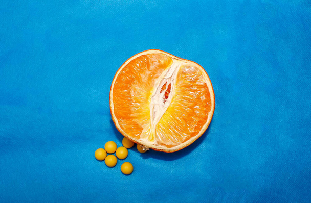 Half an orange with round vitamins of ascorbic acid lying next to it. Top view, close-up. - Fotó, kép