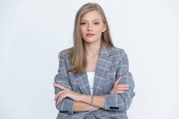 Confident businesswoman holding her arms crossed and wearing suit while sitting on white studio background - Fotografie, Obrázek