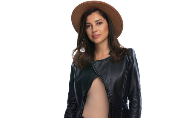 白いスタジオの背景に立っている間に帽子と革のジャケットを身に着けているカジュアル女性を確信 - 写真・画像