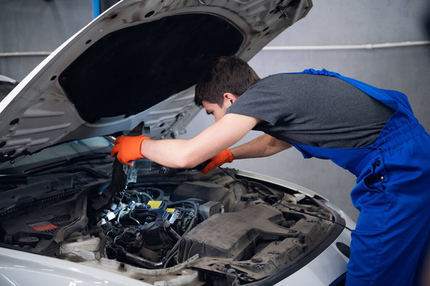 Un trabajador inspecciona un motor de coche usando una lámpara - Foto, Imagen