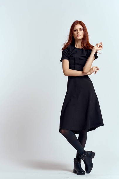 Siyah elbiseli, açık renk elbiseli, külotlu çorap ayakkabılı, kızıl saçlı ve poz veren bir kadın. - Fotoğraf, Görsel