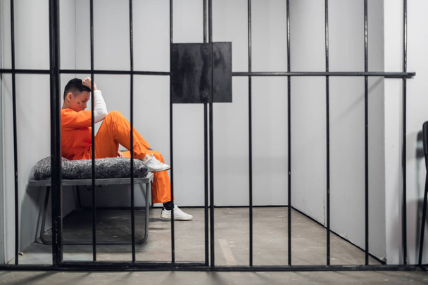 アジアの刑務所でオレンジのローブを着た犯罪者を持つ独房。コピースペース。若い男の悲しい感情. - 写真・画像