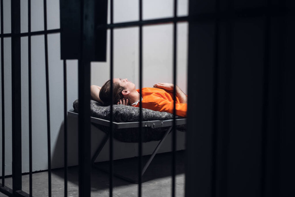 Ein gefährlicher Gefangener in einer Zelle ruht und schläft in einer Einzelzelle auf einer Liege in einem orangefarbenen Gewand. - Foto, Bild