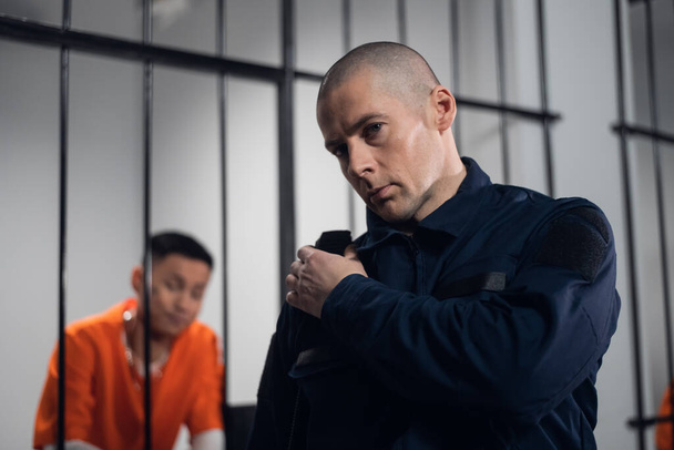 Um guarda prisional munido comunica-se com o seu parceiro no rádio. Ao fundo, um prisioneiro numa cela - Foto, Imagem