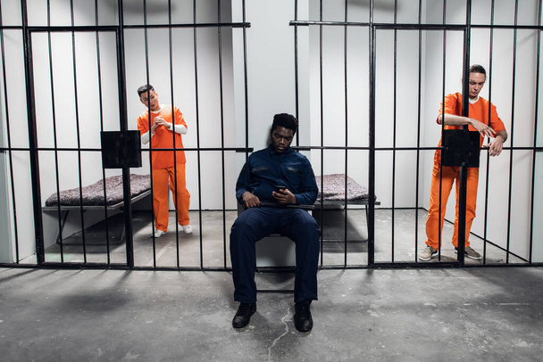Un puissant gardien de prison noir garde les cellules avec des prisonniers dans le couloir de la prison - Photo, image