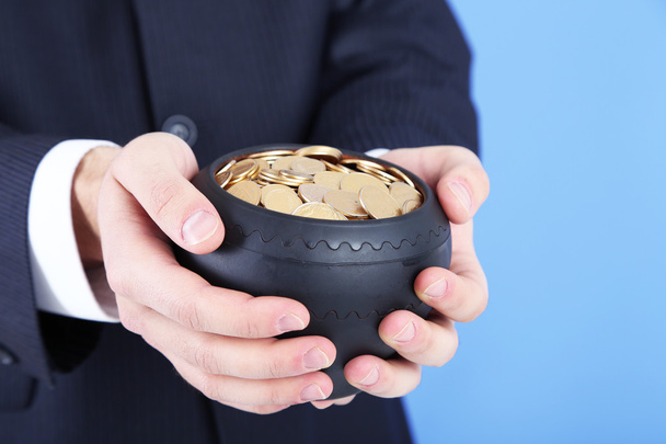 Pot en céramique avec des pièces d'or dans les mains des hommes, sur fond de couleur
 - Photo, image