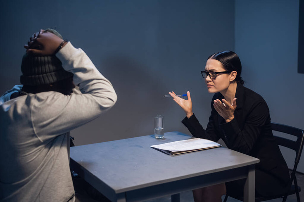 Na delegacia, uma investigadora interroga um cara negro que está sentado na frente dela algemado - Foto, Imagem