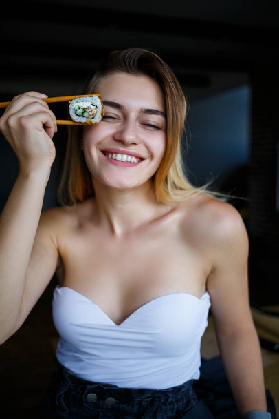 Krásná dívka jí sushi zblízka. Usmívající se žena držící sushi rolku hůlkami. Zdravé japonské jídlo. - Fotografie, Obrázek