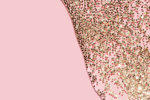 прозора рідина з золотим блискітками наливається на пастельний рожевий фон
 - Фото, зображення