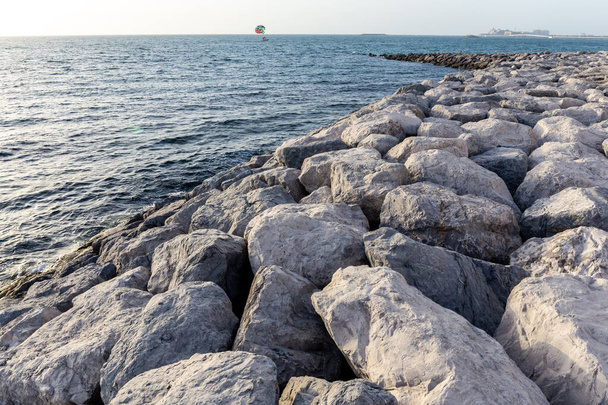 Odrzutowiec wykonany z dużych kamieni i skał sięgających do morza na wyspie Bluewaters w Dubaju. Parasailing skrzydło w tle. - Zdjęcie, obraz