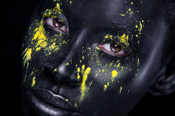 Woman with black body paint. Cheerful young african girl with art bodypaint. An amazing model with yellow makeup. Closeup face. - Фото, изображение