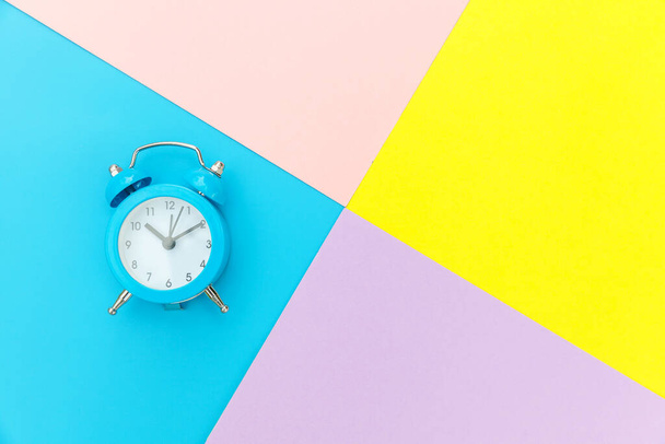 Ringing twin bell classic alarm clock isolated on blue yellow pink pastel colorful geometric background. Rest hours time of life good morning night wake up awake concept. Flat lay top view copy space - Photo, Image