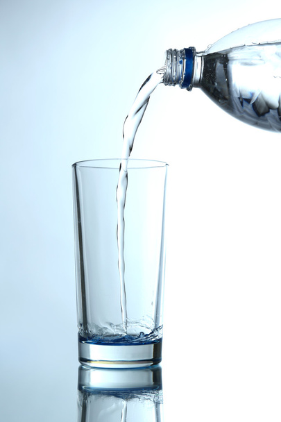 Pour water from bottle into  glass, on light blue background - Photo, Image