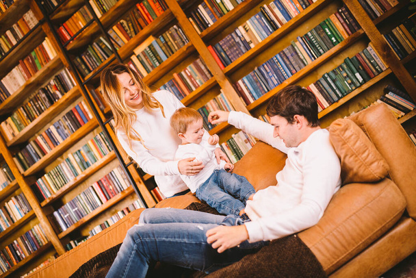 Lovely family with baby son dressed in the same clothes have fun on sofa at home during Christmas. Family Christmas Concept. Happy parents with cute child In a living room on new year holidays. - Photo, Image