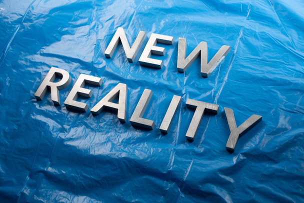 las palabras nueva realidad colocada con letras blancas sobre fondo de película de plástico azul arrugado - perspectiva inclinada - Foto, Imagen