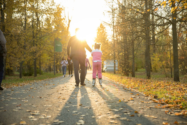 Happy family of dad and his daughter walking in the autumn park - the girl riding on the rollers - Zdjęcie, obraz